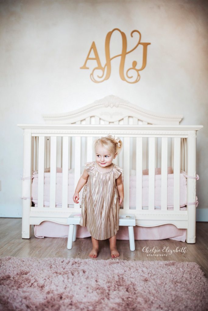 2 year old girl next to her crib
