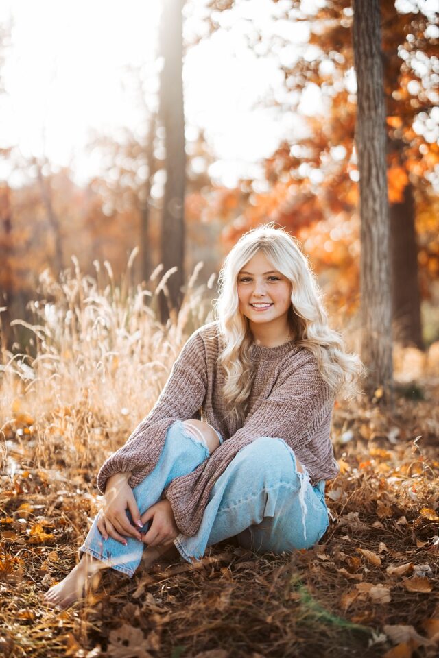 senior portrait sitting on the ground in the fall