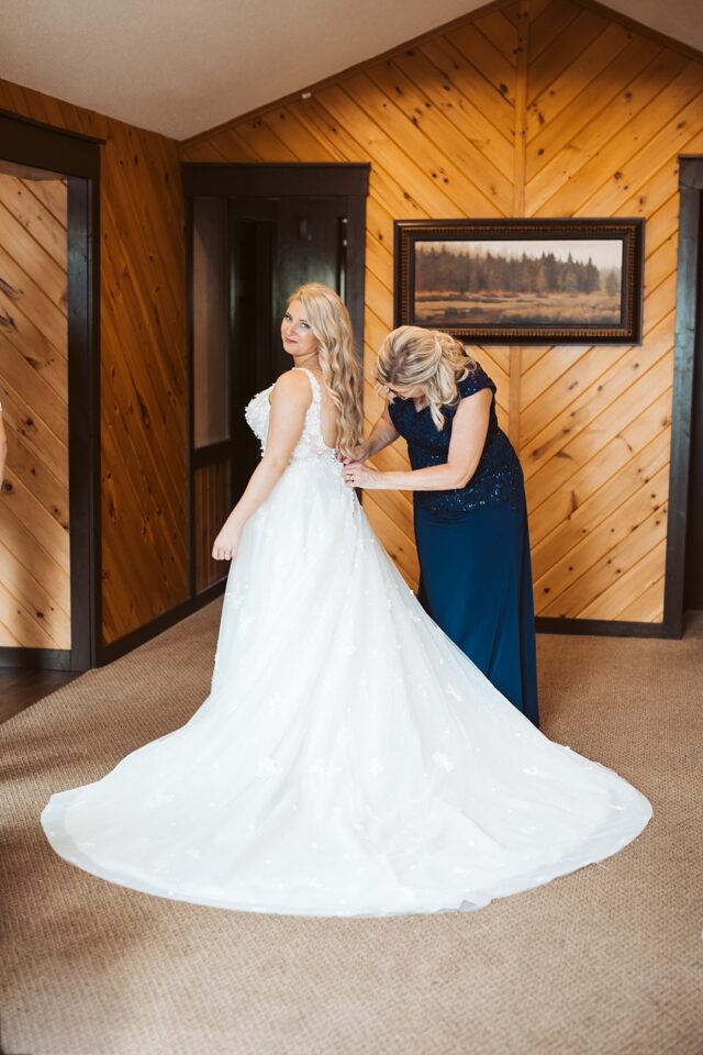 a timeless photo of a bride getting her dress zipped by her mother