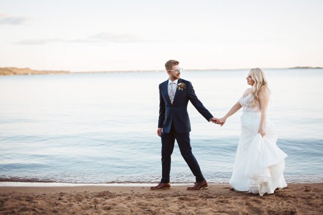 a groom and bride walking on the beach along Gull Lake in Nisswa MN