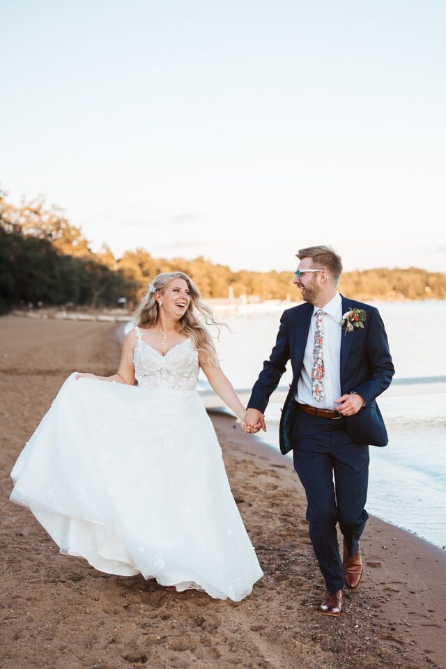 a bride and groom running on the beach at Grand View Lodge in Nisswa MN